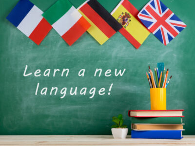 Learning languages concept - flags of Spain, France, Great Britain and other countries, blackboard with text "Learn a new language!", books and chancellery